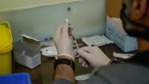 Person with gloves draws liquid from vial with syringe