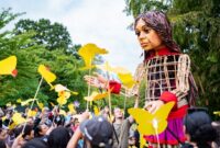 Little Amal above crowd who're holding paper butterflies