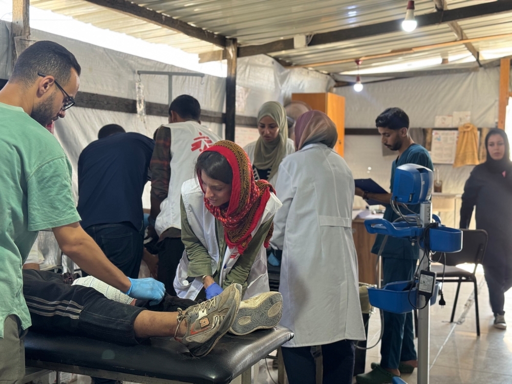 Two groups of MSF staff members gather around two hospital beds as they administer care to unseen people who need treatment for war-related injuries.