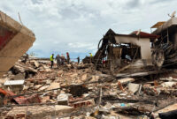Un groupe de secouristes recherchent des personnes survivantes dans les décombres d’un immeuble détruit lors du double séisme du 24 juin au Venezuela. Des débris jonchent le sol et des murs sont calcinés.